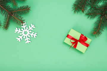 Fototapeta na wymiar Gift box, fir tree branches with decorative snowflake on green background.