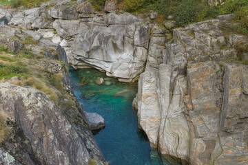 Fototapeta na wymiar Acqua blu verde scorre tra le alte rocce grigie del fiume