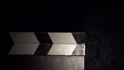 Film slate clapped in with a cloud of chalk dust. Close up. Black background
