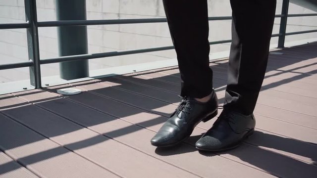 Side view of male legs in black shoes crossing bridge at normal speed. Person in black trousers making confident steps. Pedestrian concept