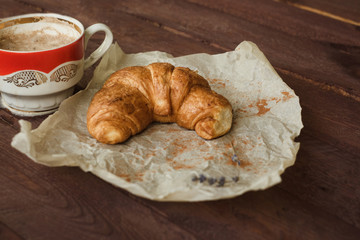 Coffee and croissant for breakfast on rustic wooden table, top view