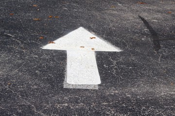 A white painted arrow on the blacktop road on a close view.