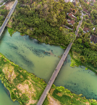 Long bridge aerial top view with wide river, green trees, and small village