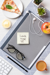 top view of sticky note with inscription lunch time, eyeglasses, earphones, pizza an apple on table