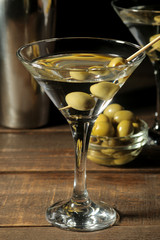 Martini in a glass wineglass with green olives on a skewer on a brown wooden table. cocktails. bar