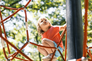 Active little child playing on climbing net the playground. A girl play and climb outdoors on sunny summer day. 