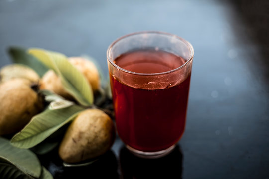 Close up of organic juice of red guava or amarood or jamrukh in a transparent glass with raw guava and its leaves on wooden surface.