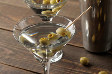 Martini in a glass wineglass with green olives on a skewer on a brown wooden table. cocktails. bar