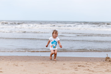 Fototapeta na wymiar A little girl having fun near the sea, running. A gloomy cloudy day at the sea