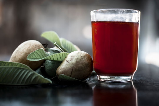 Close up of organic juice of red guava or amarood or jamrukh in a transparent glass with raw guava and its leaves on wooden surface.