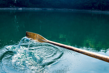 Oar of boat touching water and causing splash and ripples in the water A wooden paddle on a boat Blade of wooden kayak or canoe paddle Water splash  
