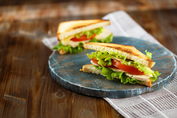 Appetizing sandwich with chicken, tomatoes, lettuce, cheese on a wooden plate on a dark background