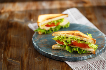 Appetizing sandwich with chicken, tomatoes, lettuce, cheese on a wooden plate on a dark background