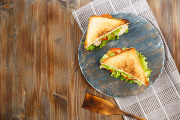 Two tasty sandwich with chicken, tomatoes, lettuce, cheese on a wooden plate on a dark background