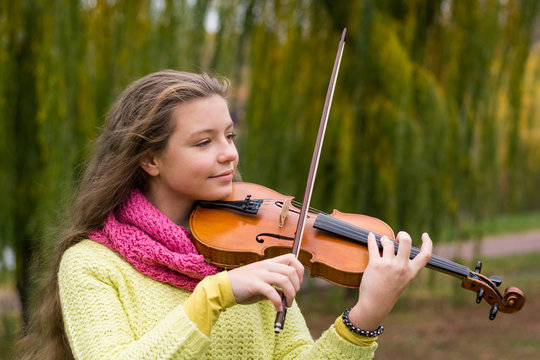 Girl playing the violin eyes closed in the autumn park at a lake and willow foliage background.