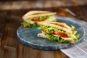 Two tasty sandwich with chicken, tomatoes, lettuce, cheese on a wooden plate on a dark background