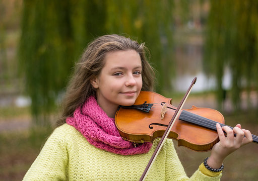 Girl playing the violin in the autumn park at a lake and willow foliage background.