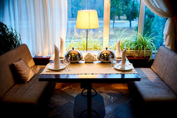 Setout table with a hot dish under the cloche near the window in the restaurant.