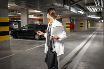 Young business woman walking with car keys in the underground parking of the new residential...