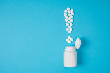 White pills in a exclamation mark poured from a medicine bottle on blue background. Medication and...