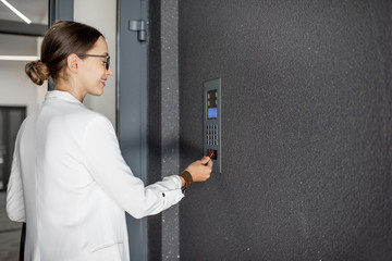 Young business woman in white suit touching the intercom with keychain opening the door of...
