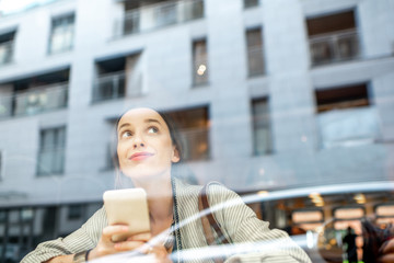 View through the window on the stylish woman sitting indoors with modern building on the reflection. Wide view with copy space