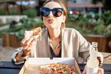 Young woman having a snack with pizza sitting outdoors at the modern public park