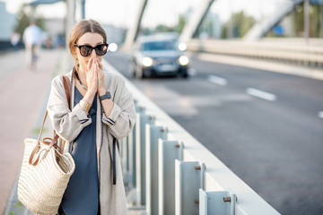 Woman closing her nose feeling bad because of the air pollution on the bridge with traffic in the...