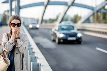Fototapeta premium Woman closing her nose feeling bad because of the air pollution on the bridge with traffic in the city