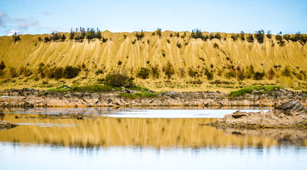 Sandy hills. Lake in the Sandy canyon. Warm colors background. Yellow sandstone textured mountain, white thin sand dune, bright sky. Sunshine landscape