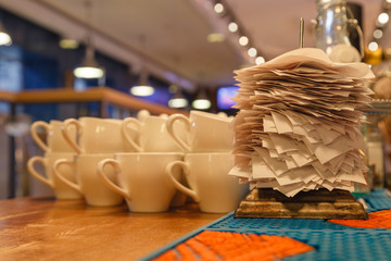White ceramic mugs for tea and checks from completed orders in the bar or restaurant kitchen impaled on a sharp thin iron needle on stand. Concept checker, stand for checks, checkbox