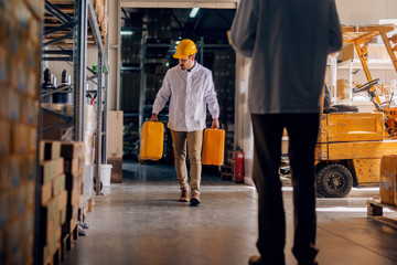 Fototapeta premium Worker carrying water tanks. Warehouse interior.