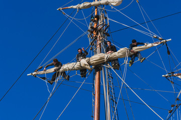 Sailors work with sails at a height on a traditional sailboat