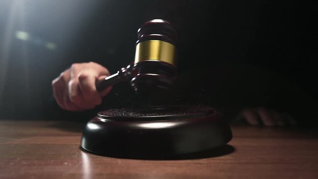 Judge hitting Gavel off a block in courtroom, dark background slow motion shot