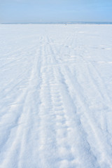 Traces of sledge runners and ski on white freshly fallen snow on winter frozen lake.