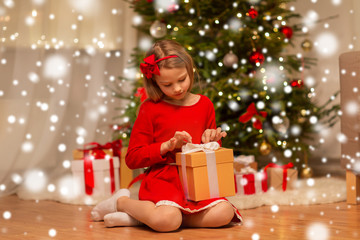 christmas, holidays and childhood concept - girl in red dress with gift box at home