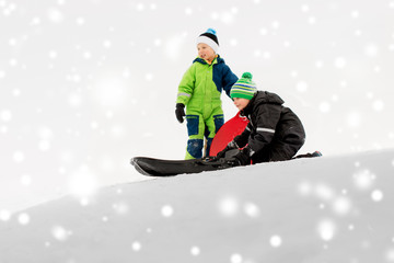 Fototapeta na wymiar childhood, sledging and season concept - little kids sliding on sleds down snow hill in winter