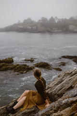 Fototapeta na wymiar woman with long braid sitting on a foggy rocky coast