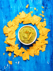 Fresh guacamole sauce in bowl with Mexican corn chips over blue background, top view.