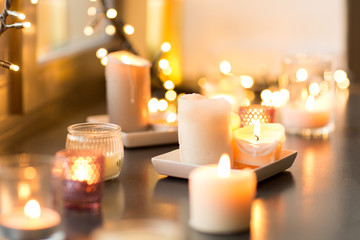 hygge, decoration and christmas concept - candles burning in lanterns and festive garland on window...