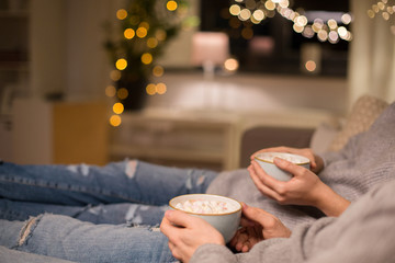 hygge, leisure and christmas concept - close up of couple drinking hot chocolate with marshmallow...