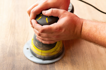 Closeup of hands holding a manual grinding machine. Sanding a wooden surface.