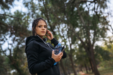 Fototapeta premium Woman jogger holding water and smart phone while exercising in park