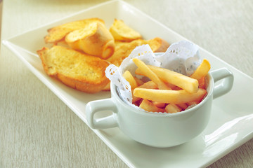close-up of french fries in cup with garlic bread on wood table in restaurant