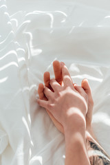 partial view of loving couple holding hands while lying on white bed sheet