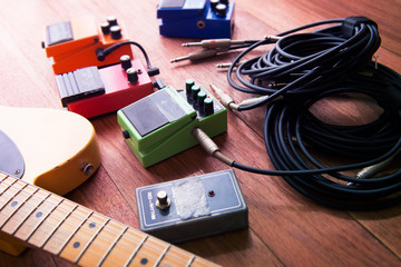 Setting up guitar audio processing effects. Electric guitar and stomp box type effectors and cables on studio floor. Intentionally shot with impressional feel, color and tone.