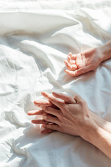 partial view of couple in live holding hads while lying in bed together