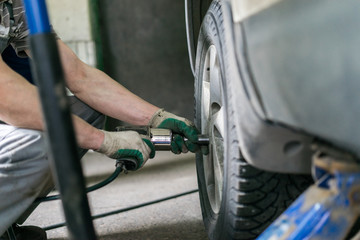 Fototapeta na wymiar car mechanic screwing or unscrewing car wheel of lifted automobile at repair service station