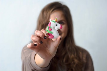 close up  toy unicorn in the hands of a woman on a white wall background