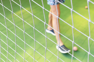 Football net close up on blurred green grass football field and male feet playing a small ball background